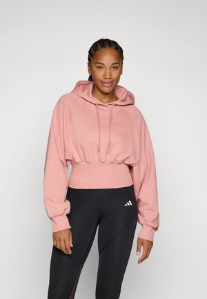 Krótka różowa bluza z kapturem regulowanym sznurkiem, ściągaczami u dołu i długimi rękawami, połączona z czarnymi legginsami z białym logo.