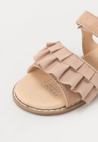 Beige mockasinsandaler med en rynkad rem, öppen tådesign och platt sula. Diskret sömnad och ett tryckt logotyp på innersulan.