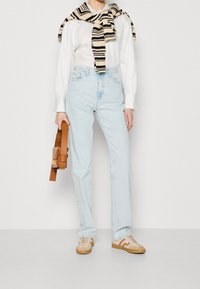 Ljust blå höga jeans, vit långärmad skjorta, randig stickad tröja hängande, brun läderhandväska, beige sneakers med bruna accenter.