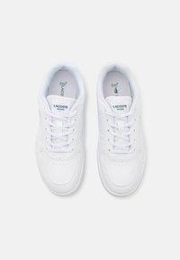 Sneakers bianchi in pelle sintetica con punta rotonda, allacciatura frontale e delicate perforazioni. Presentano dettagli del logo verde sulle solette.