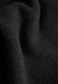 Tessuto nero con una superficie morbida e pelosa, caratterizzato da una leggera elasticità e un motivo di tessitura irregolare, che conferisce una ricca profondità.