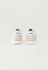 Bež antilop superge z belimi detajli in gumijastimi podplati. Imajo oblazinjen ovratnik in oznako na peti s logotipom "Reebok".