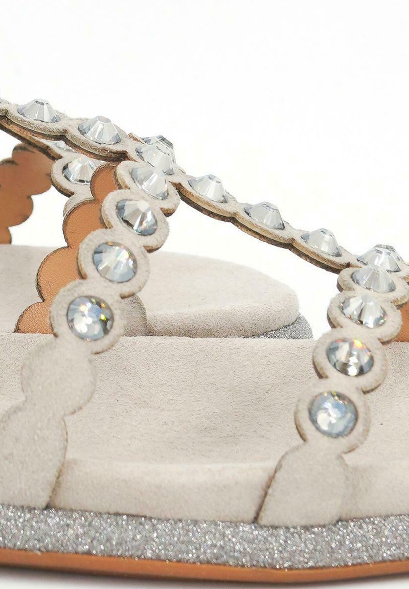 Sandalias de ante beige con tiras onduladas adornadas con cristalitos transparentes, con una suela plateada brillante y una plantilla de textura suave.