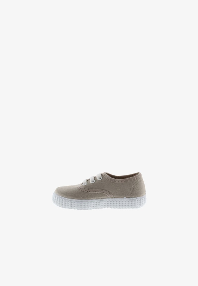 Zapatilla de lienzo beige con suela de goma blanca, puntera redonda y tres ojales. Presenta un detalle de costura sutil en los lados. Diseño compacto.