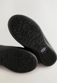 Soli negri de pantofi cu un model texturat de inimi, având un logo "next" violet pe unul dintre ele. Finisaj neted și formă rotunjită.