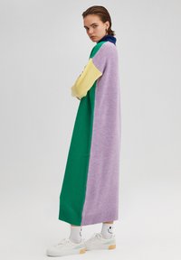Robe en tricot avec un col montant, présentant des couleurs en blocs : vert, violet et jaune. Coupe longue et ample avec des poignets côtelés et un ourlet uni.