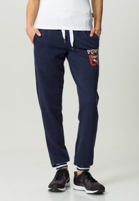 Navy cotton sweatpants with white drawstring, featuring a red and white graphic logo print on the left thigh, ribbed ankle cuffs.