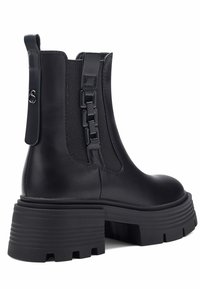 Botas de cuero negro hasta el tobillo con paneles laterales elásticos, un detalle de cadena en la parte posterior y una suela gruesa con textura para mayor tracción.