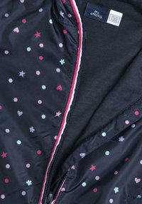 Vnitřek námořnické bundy s puntíkovaným vzorem v růžové, modré a bílé barvě, zdobený srdíčky a hvězdami. Obsahuje růžovo-bílý pruhovaný zip.