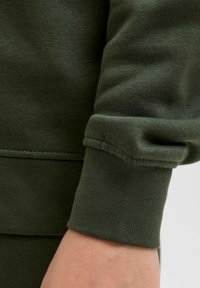 Mörkgrön sweatshirtärm med ett mjukt, blandat bomullstyg. Muddarna är ribbade med sydda sömmar för hållbarhet.