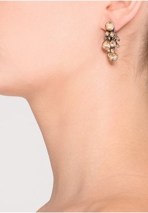 Boucles d'oreilles pendantes en ton or avec plusieurs pierres précieuses rondes d'ambre portées à l'oreille gauche d'une personne, avec le côté du cou visible.