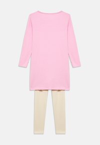 Ροζ βαμβακερή τουνίκ με μακριά μανίκια και στρογγυλή λαιμόκοψη, συνδυασμένη με κρεμ κολάν, και τα δύο με απαλή, λεία υφή.