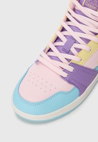 Sneaker colorido com biqueira rosa pastel, acabamento azul, painéis roxos e amarelos, atacadores rosa e logótipo dourado da Kappa na lingueta.