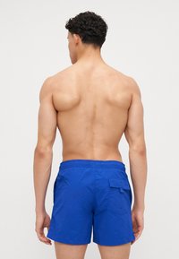 Shorts de bain bleus en tissu léger, dotés d'une taille élastique et d'une poche arrière, conçus pour le confort et la liberté de mouvement.