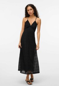 Robe maxi en dentelle noire avec des bretelles fines, décolleté plongeant et un motif détaillé. Présente une silhouette fluide et une fente latérale pour plus de mouvement.