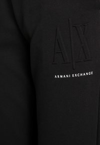 Svart bomullströja med strukturerad sömnad och djärva präglade logoinitialer "AX" samt "ARMANI EXCHANGE" i vitt nedanför.