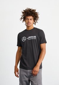 Czarna bawełniana koszulka z krótkim rękawem z okrągłym dekoltem, z białymi logo Mercedes-Benz oraz zespołu AMG Petronas Formula One Team.
