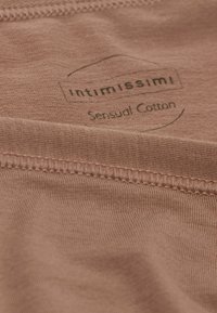 Close-up van een zacht, perzikkleurig stof met het label "Intimissimi" en de tekst "Sensual Cotton" erop gedrukt.