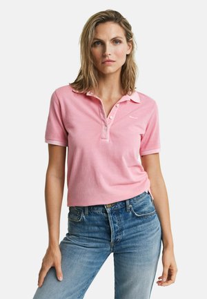 Roze katoenen polo met een drieknoopsluiting, logo op de linkerborst en opgerolde mouwen, gecombineerd met lichtblauwe spijkerbroek.