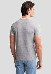Camiseta gris de manga corta con escote redondo y ribetes en contraste en las mangas, combinada con jeans de color azul claro. Textura de tela suave.