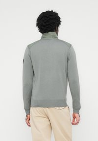 Light gray sweater with a high collar, ribbed cuffs, and hem. Features darker gray shoulder panels. Soft knit fabric, minimal design.