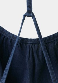 Tissu en denim bleu foncé avec couture froncée et deux fines bretelles nouées en nœud au centre supérieur.