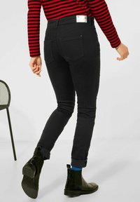 Svarta jeans i slim fit, med bakfickor, en silverdekoration vid midjan och uppvikta ärmar. Bärs med svarta stövlar.