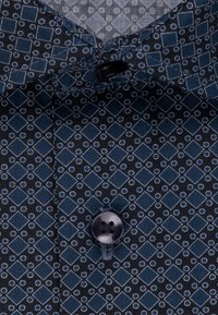 Camisa navy de botones con un patrón geométrico de diamantes y círculos en azul claro, con un botón negro y tela texturizada.