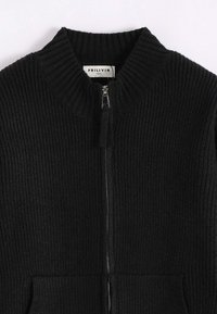 Veste noire en tricot avec une texture côtelée, col montant et fermeture éclair frontale. Comprend deux poches latérales et une étiquette à l'intérieur indiquant la marque et la taille.