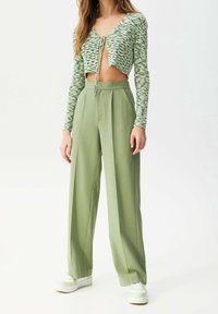 Haut court en maille avec motif vert et blanc, col en V profond, et lien à nouer à l'avant ; pantalons taille haute à jambes larges en vert clair uni, avec plis.
