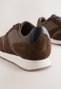 Baskets en daim et cuir marron avec une finition texturée, une semelle intermédiaire blanche et un design à bout arrondi. Présentent des accents en cuir foncé au talon.