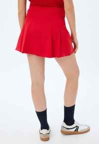 Minifalda corta roja con pliegues, tejido suave, cintura ajustada, se ensancha en el dobladillo. Combínala con zapatillas blancas y calcetines azul marino para un look casual.