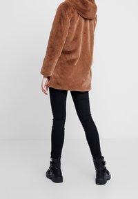 Brown fuzzy coat with a hood, loose fit, and long sleeves, paired with black leggings and buckle-accented black boots. Smooth textile.