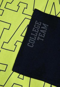 Żółta bawełniana tkanina z dużymi graficznymi literami. Ciemnoniebieska łatka wyświetla tekst "ZESPÓŁ KOLEŻEŃSKI" w szarym kolorze.