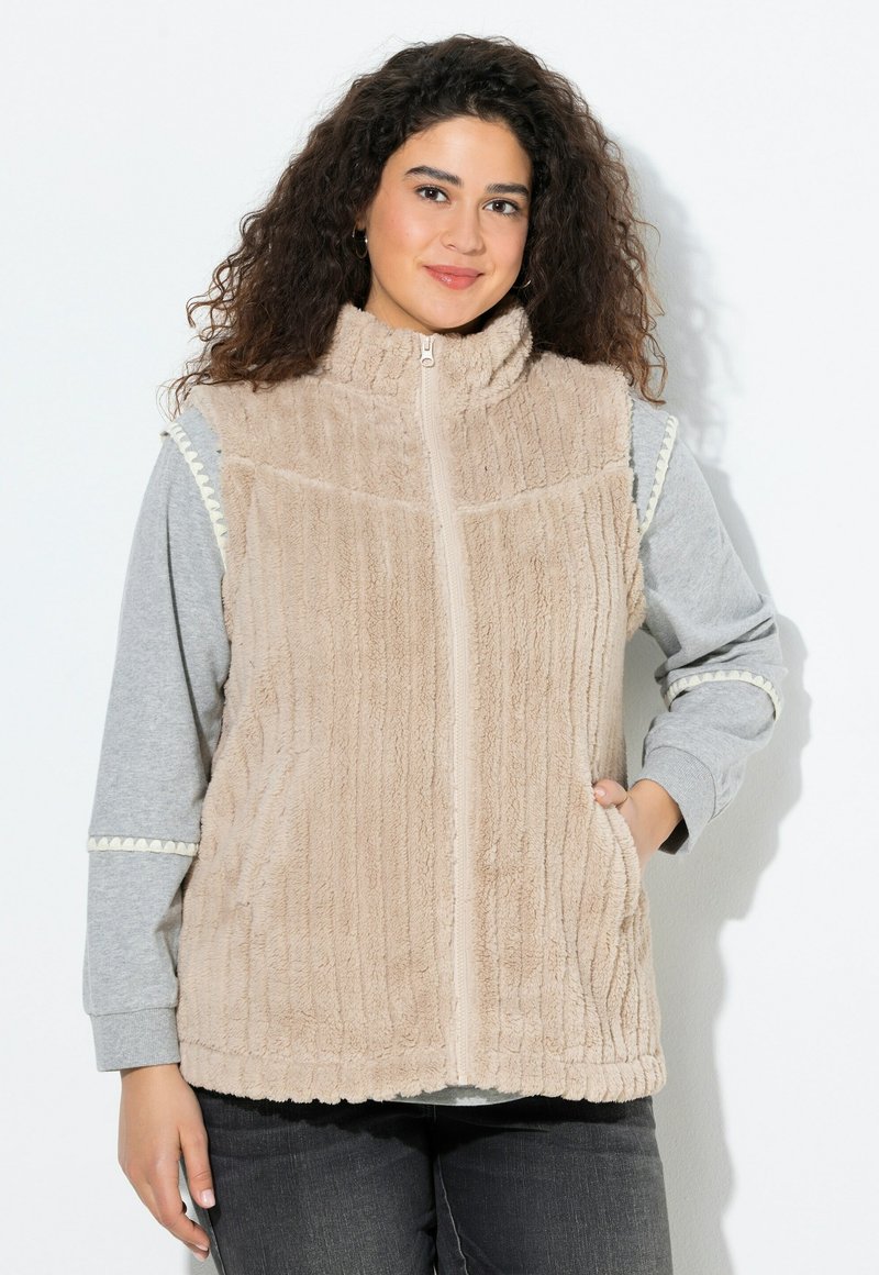 Gilet en polaire beige avec col montant et fermeture éclair à l'avant. Il présente une texture côtelée et des poches. Porté par-dessus une chemise à manches longues grise.