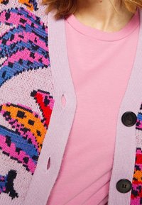 Strikket cardigan i pink med farverige dyreprint-detaljer, parret med en ensfarvet pink t-shirt. Har knaplukninger og ribbet tekstur.