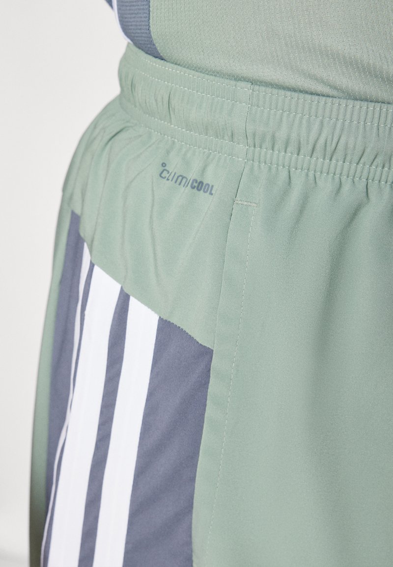 Pantalones cortos atléticos verdes de material ligero, con paneles laterales grises y franjas verticales blancas, y un logo de ClimaCool.