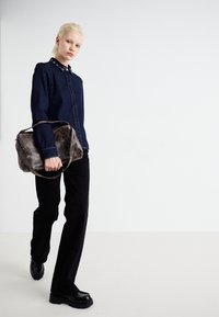 Denim shirt with snap-button collar, black straight-leg pants, and shiny black shoes. Carrying a textured gray bag with a long strap.