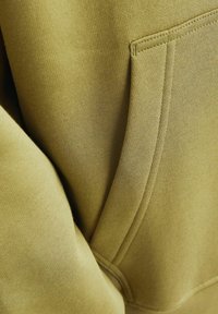 Olivenfarbener Hoodie-Stoff mit einer weichen Textur, der über eine Vorderseite-Tasche und gestickte Details entlang der Kanten verfügt.