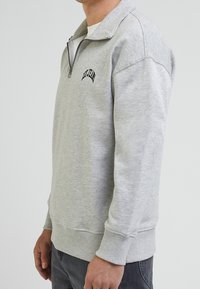 Grijze sweatshirt met een halve rits kraag, geribde manchetten en zoom, met zwart geborduurde tekst op de voorkant en een zachte, gestructureerde stof.