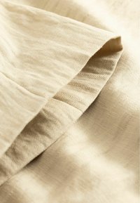 Gros plan sur un tissu beige plié avec une texture subtile en chevrons et des ombres douces mettant en valeur les plis.