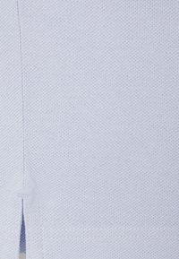 Hellblauer Stoff mit einem strukturierten, gestrickten Muster. Verfügt über einen kleinen seitlichen Schlitz und flache Nähte, die ein sauberes, einfaches Design bieten.