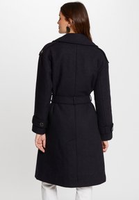 Donkerwollen trenchcoat met een ceintuur in de taille, grote kraag en knoopmanchetten, met een gestructureerde afwerking en een middellange snit.