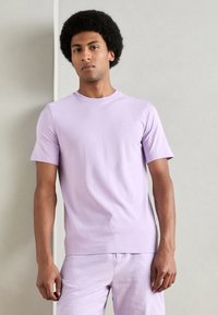 Lavendel t-skjorte med korte ermer i myk bomull, med rund hals og en liten brodert logo på brystet, sammen med matchende bukser.