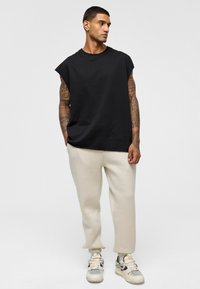 Zwarte mouwloze t-shirt, relaxte pasvorm, gecombineerd met beige joggerbroeken met boorden bij de enkels, afgewerkt met lichtgekleurde sneakers en zichtbare patronen.