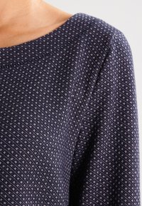 Marinblått mönstrat tyg med små, ljusa diamantformer. Slät textur och mjukt fall, med vid halsringning och korta ärmar.