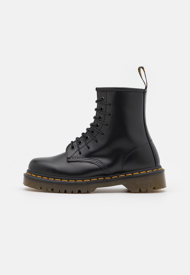 Bottine en cuir noir avec huit œillets, couture jaune sur une semelle épaisse marron à rainures et boucle de tirage à l'arrière.