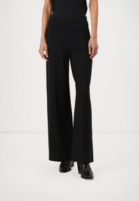 Black, wide-legged trousers with a smooth texture and high waistband, designed for a loose fit. Worn with black ankle boots.