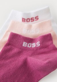 Three pairs of ankle socks in white, light pink, and dark pink, featuring ribbed texture and "BOSS" logo in contrasting colors on cuffs.