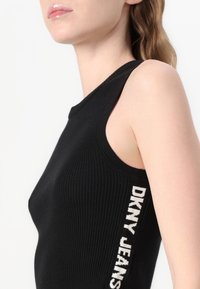 Fekete bordás, ujjatlan felső kerek nyakkivágással és fehér "DKNY JEANS" logóval az oldalon. Sima anyagú, testhez simuló fazon.
